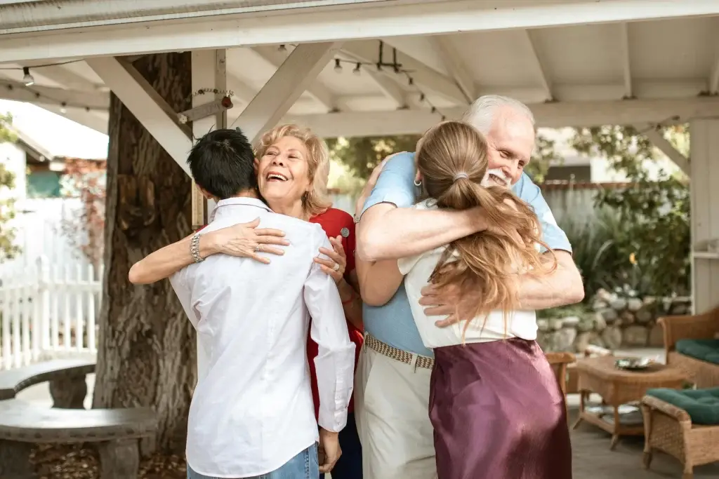 Image of 2 elderly parents hugging their kids after having the talk about downsizing.